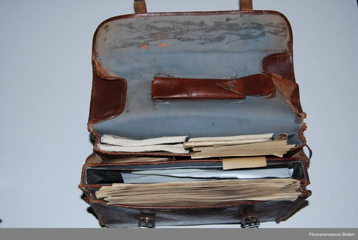Utvikbar väska av brunt läder med låsbar låda av bleckplåt i botten, nyckeln saknas. Innehåller blanketter, kuvert, linjal m.m. (moderna utgåvor). Se AM.078470 för modellexemplar.