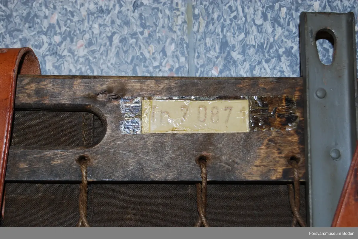 Träram med nät och vikta smärtingöverdrag hopspända med remmar. Lyfthandtag av läder på vardera sidan. Två skenor av järn med hål i änden sitter monterade på varje ram. Materielnr Tn 70871, senare nr M7951-708710.