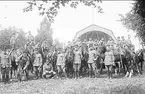 Avdelning under rast. Soldaterna är iklädda uniform m/1910 och mössa m/ä. Även furiren längst fram till höger har uniform m/1910. I bakgrunden till höger syns musikpaviljongen och till vänster del av syrénbersån i vilken K 3:s dansbana låg.
