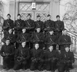 Grupporträtt av elever vid korpralskolan på F 2, 1944. Flygplansmekaniker utrustade med vapen vid trappa.