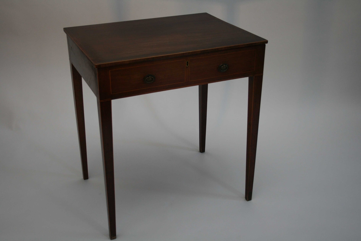 Polert mahognibord med intarsia. Rektangulær plate, avsmalende bein og to falske skuffer i sargen. Bordplata kan slås opp, og under er det et lite skyvespeil og 9 små rom, 6 rom har lokk.