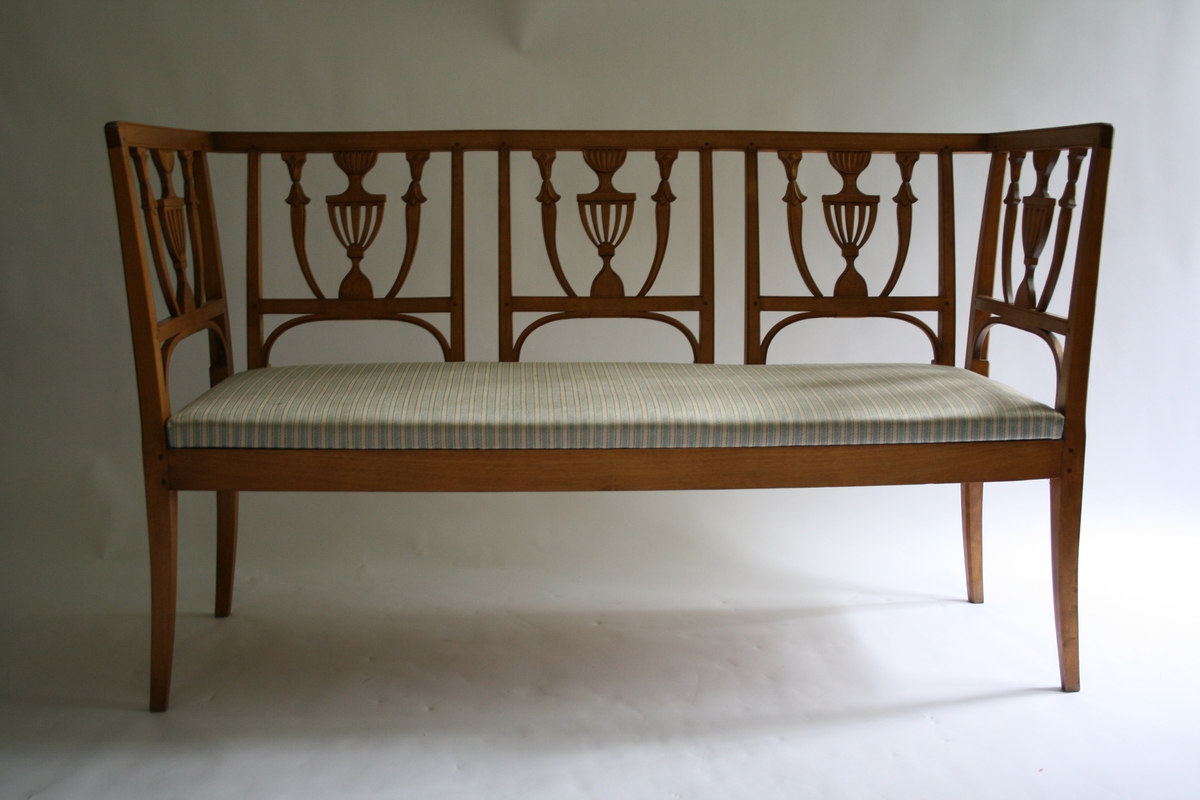 3-sete bjerkesofa i empirestil med ryggbrikke utformet som en urne. Løst sete med stripete trekk, lys blått og lys grått like striper med en mørkere grå tråd innimellom, håndvevet.