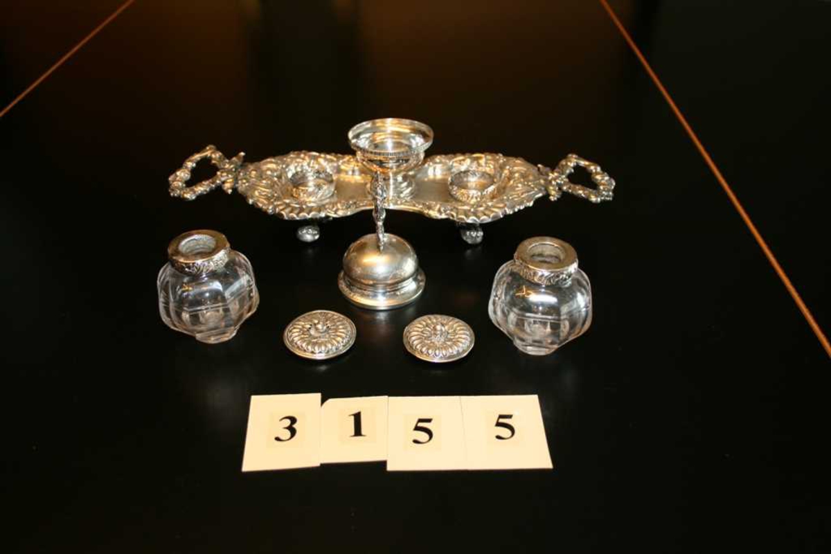 Avlangt sølvbrett, på fire føtter. To håndtak, innsvinget på midten, ornametikk med blomster og rocailler. Skål med bjelle festet midt på brettet, på hver side er det holdere til blekkhus og sandhus. Disse er av glass med kant og lokk av sølv.