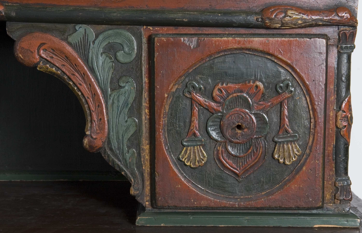 Framskap på fire dreide ben. Dekorert med marmorering, utskårne klassisistiske motiv og krone med gjennombrutt akantusranke.