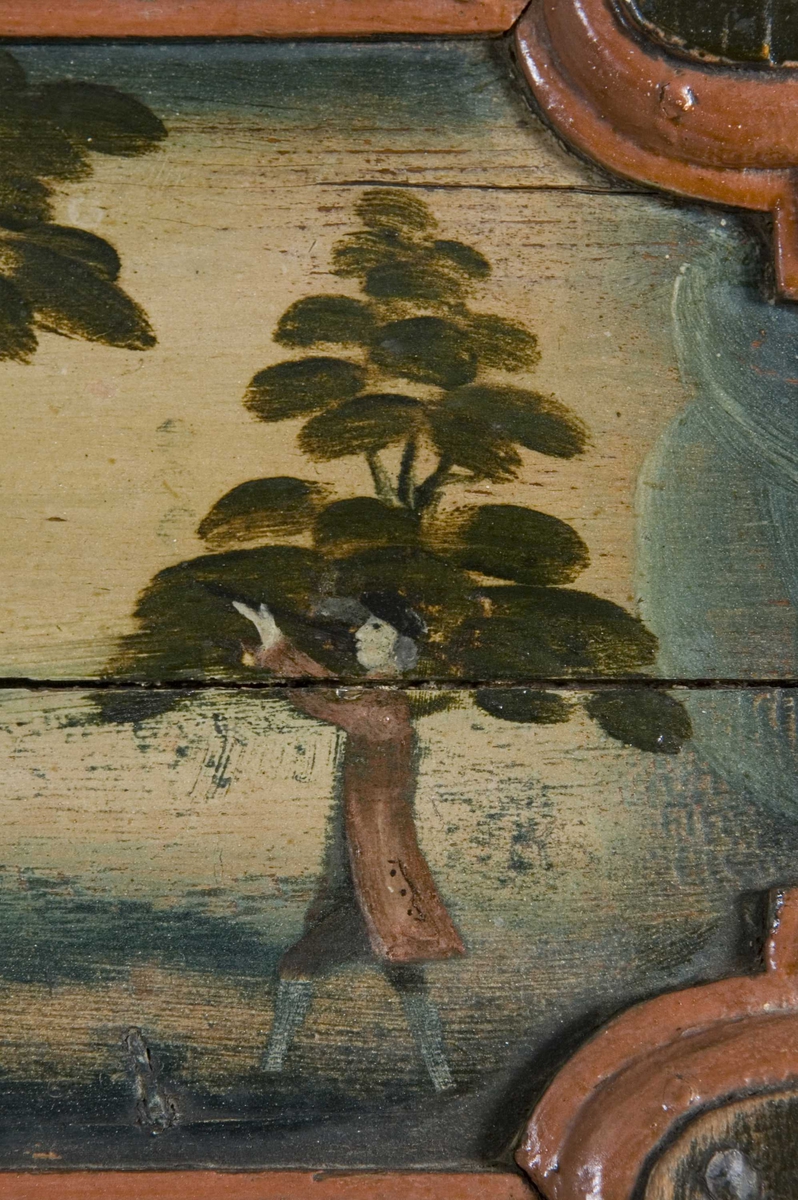 Flatskap med doble dører og klaff i overkant, hengslet på undersiden. Dekormalt med landskapsmotiver i feltene.