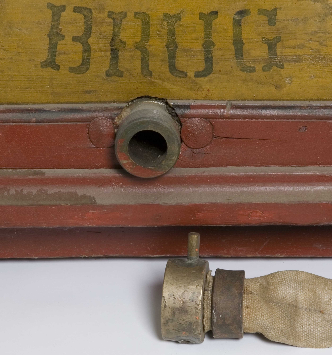 Trekasse med pumpesylinder og håndtak i to sider. Kobling for slange i nedkant av kassen. Malt rød med gule fyllinger og svart mekanikk.