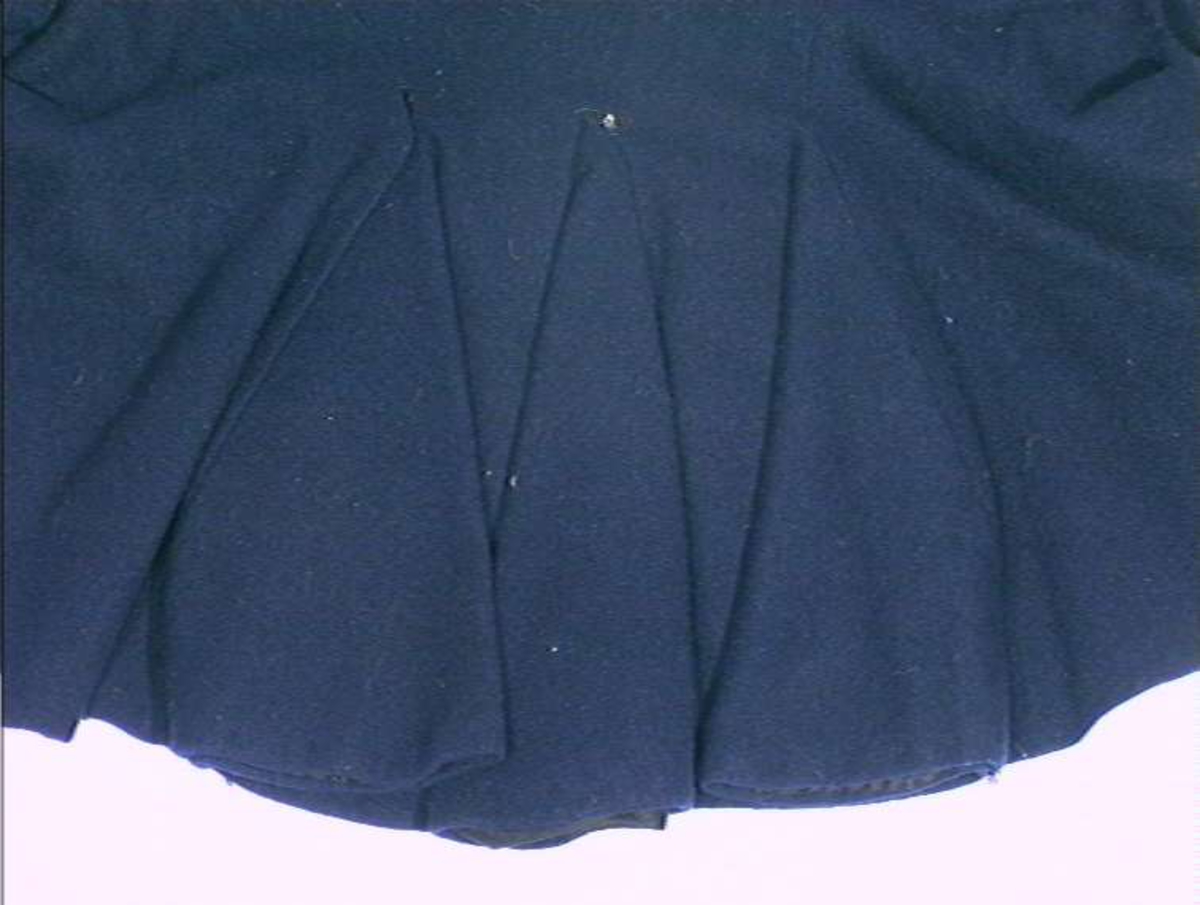 Mørkeblå trøye i ull, maskinsydd. Dekor av 3 cm brede bånd langs fremkanter, hals og ermeringning.I rygg nederst er det 3 innfeldte trekanta kiler som er foret med linlerret og bomullsstoff.