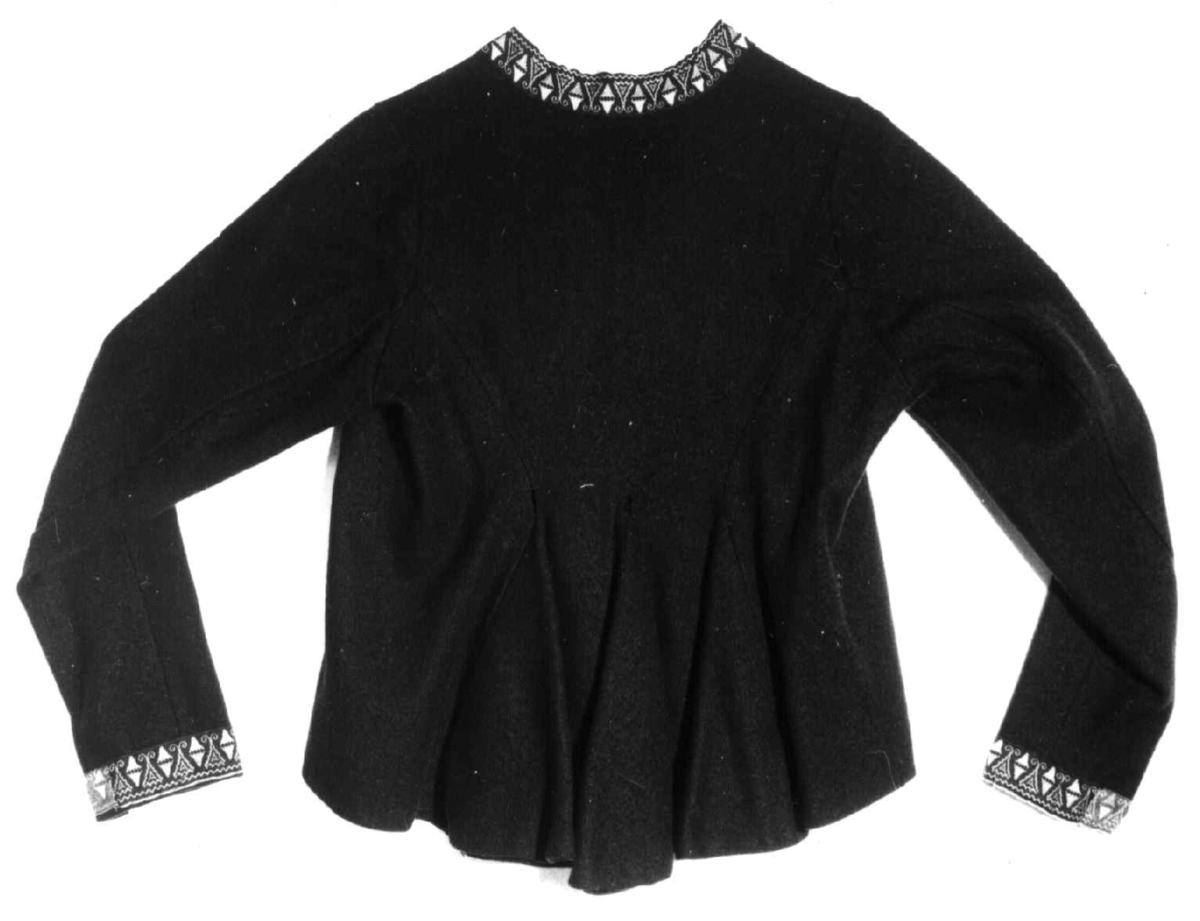 Mørkeblå trøye i ull, maskinsydd. Dekor av 3 cm brede bånd langs fremkanter, hals og ermeringning.I rygg nederst er det 3 innfeldte trekanta kiler som er foret med linlerret og bomullsstoff.