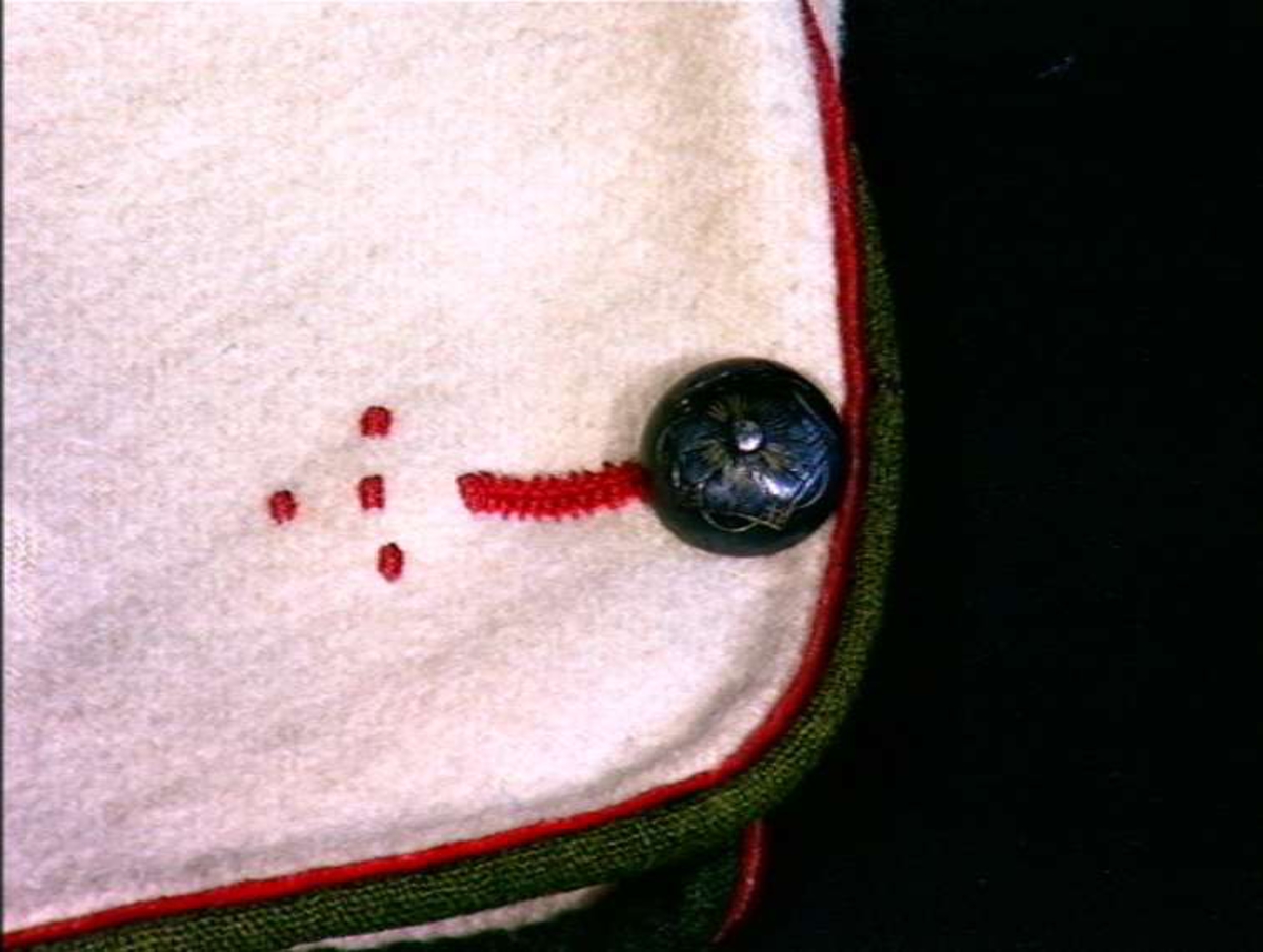 Gråtrøye av ull med grønn og rød kantinger.
I ermesplitter 1 par sølv knapper.