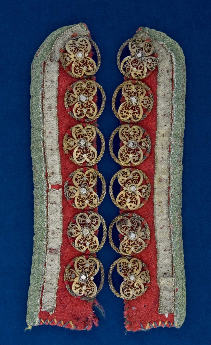 Maleklut med bredt sølvbånd sydd oppå rødt ullstoff foret på baksiden med tynt rutete ull/linstoff. Påsydd forgylte maler med heng,