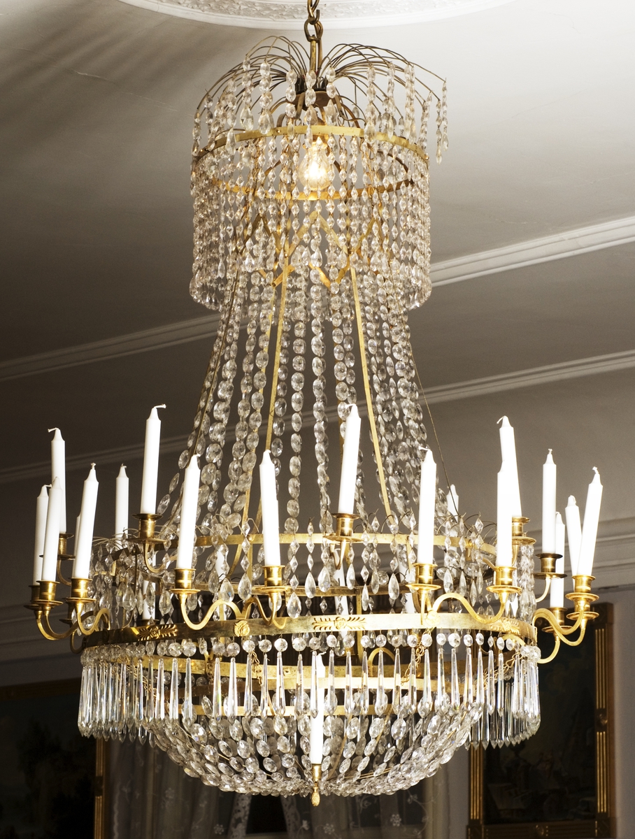 Lysekrone; glass, lenker med gjennomskinnlige, slepne, ufargede perler, bronse. Hjulkrone, fire ringer, nedre midtring har åtte dobbelte lysholdere; øvre åtte enkle. Fallende lenker fra topp til øverste midtring, andre lenker fra nedeste midtmidtring samles i bunnen av en bronserosett med lysholder. Baldakin.
