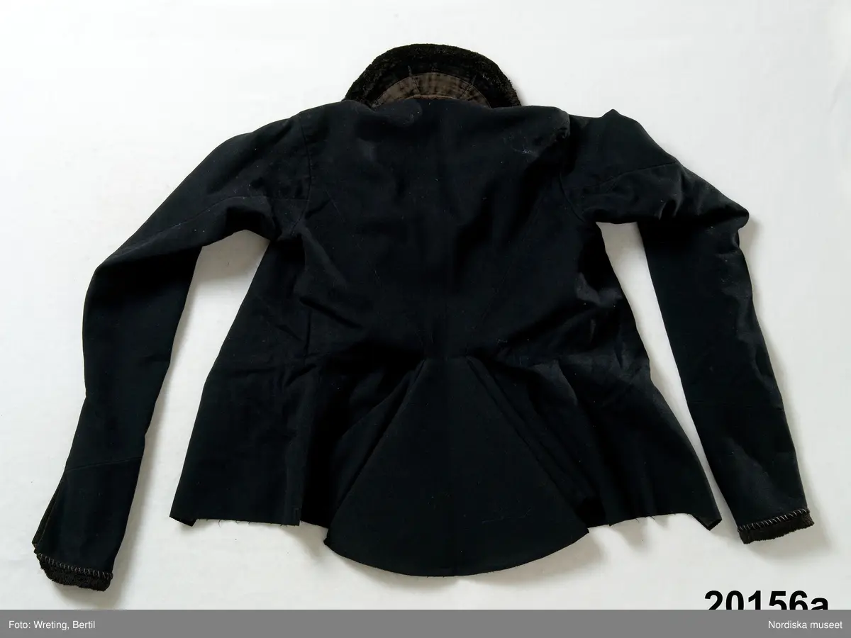 Huvudliggaren:
"Hollands draegt fr. Köpenhamn
Bestående af:
a) Kafetröje med Spaender [tillägg i blyerts.] skall vara kravetröje - 30 kr [spännet ommärkt till e+ 2011-03-08]
Spännet märkt: M.H.P.D.
b) Skjört - 28 kr
c) Forklaede med spaender - 30 kr
d) Haette med tillbehör och Haandstycke - 6 kr
e+) [spännet ommärkt till e+ 2011-03-08] Spännet märkt: M.H.P.D.
Ink. ss 20.087 [=ink. hos fru m. Wildschiödz i Köph. ss 20.001 [= gm (genom) dr A. Hazelius i Stockholm.]]- 94 kr. Under hösten 1877."
