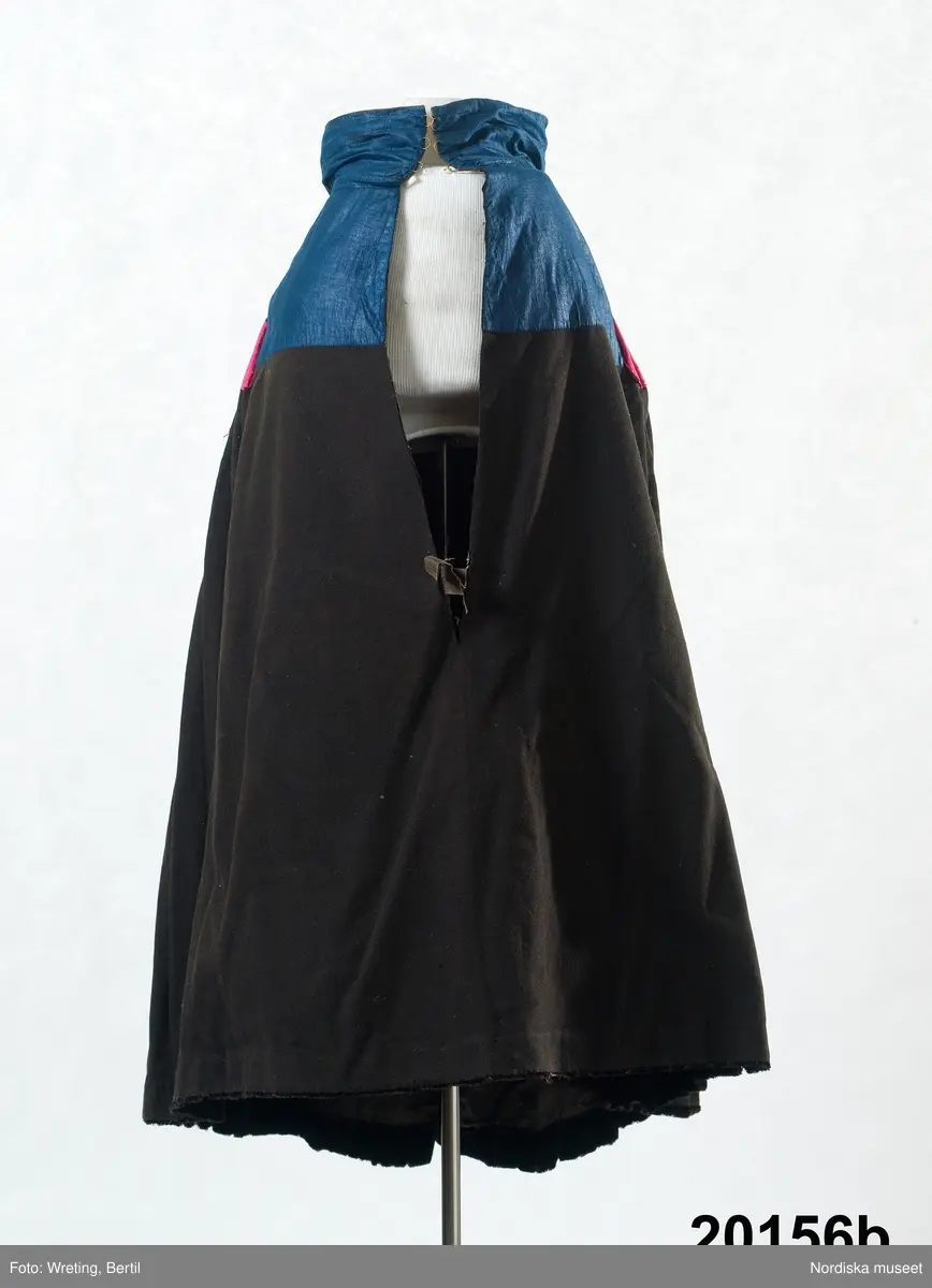 Huvudliggaren:
"Hollands draegt fr. Köpenhamn
Bestående af:
a) Kafetröje med Spaender [tillägg i blyerts.] skall vara kravetröje - 30 kr [spännet ommärkt till e+ 2011-03-08]
Spännet märkt: M.H.P.D.
b) Skjört - 28 kr
c) Forklaede med spaender - 30 kr
d) Haette med tillbehör och Haandstycke - 6 kr
e+) [spännet ommärkt till e+ 2011-03-08] Spännet märkt: M.H.P.D.
Ink. ss 20.087 [=ink. hos fru m. Wildschiödz i Köph. ss 20.001 [= gm (genom) dr A. Hazelius i Stockholm.]]- 94 kr. Under hösten 1877."

B. Kjol, "skjört"  av svart klädesberedd vadmal helfodrad med svartfärgad glättad linnelärft. Kjolkanten skodd med 4,5 cm bred svart ylleschagg. Upptill på kjolen ett 19 cm stycke av mellanblå glättad bomullslärft s.k. domestik, som bak är hårt styvat och ligger i jämna rynkor som en stel rundad platta som i nedre kanten har ett påsytt 7 cm brett rött ripsband av siden. 11 cm bred midjelinning av det blå tyget, mitt fram sprund med 3 par snöröglor av mässing i linningen.
Kjolen handsydd av material som förefaller att vara från 1700-talets andra hälft. 
Just denna typ av kjol kalls "Jöb" och bars vid sorg, Kjolen kunde då slås upp över huvudet så att den styva bakdelen fälldes upp som en solfjäder på ryggen. Se vidare Elna Mygdal: Amagerdragter, Kphmn 1930 sid 88 ff.
/Berit Eldvik 2011-11-24