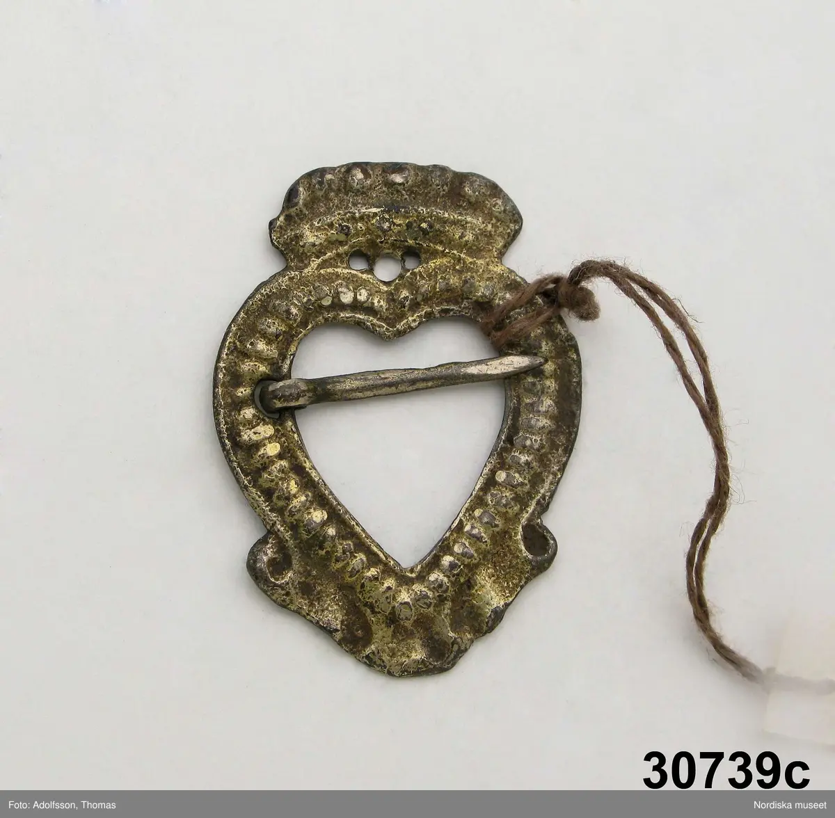 Huvudliggaren:
"a-e, Spännen. från Kalmar län. Af silfver.
Ink. gm friherre Emanuel Cederström [...]. 1/5 1881"

b) "Sölja, silfver, förgyld. H. 3,4 cm, Br 2,5 cm. Stämpel saknas. Frånsidan oförgyld."
c) "Sölja, Silfver, förgyld, gjuten. H 3,6 cm, Br 2,6 cm. Stämpel saknas. Frånsidan oförgyld."

A:1-2 Fyrkantigt halslås, helt förgyllt eller möjligen av mässing, graverad dekor i 1700-talsstil med punsad kant. Fäste för 3 kedjor som alla saknas.
/Berit Eldvik 2007-02-27 