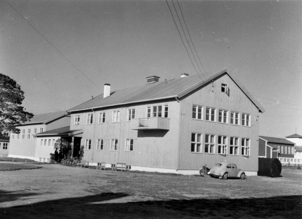 Skoler i Karasjok, del av Den Samiske Folkehøyskole, 1956, tegnet av ark. Bugge, Molde. I bakgrunnen et glimt av folkeskolen.  I 1956 var det  ikke ungdomsskole på stedet, og i 1961 var faktisk Karasjok den første i Norge som fikk linjedelt ungdomsskole. Bygget til DSF er senere brent ned og erstattet av et nytt bygg. 