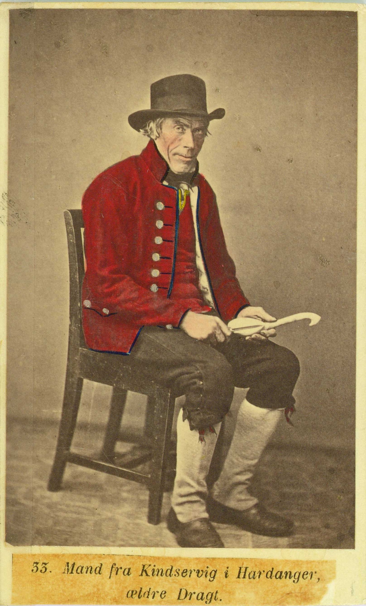 33. Mannsdrakt, Kinsarvik, Ullensvang Portrett av mann med hatt (treskjærer?) sittende i fotoatelier med nøytral bakgrunn og mønstret gulvteppe.
Fra serien "Norske Nationaldragter" (nr.33), fotografert av fotograf Marcus Selmer (1819-1900), Bergen.