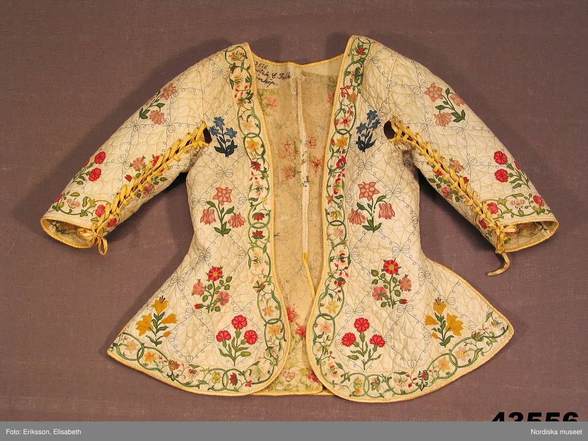 Katalogkort IV:
"Tröja / kofta, för dam, 1600-talets slut.
Längd 54 cm
Av linnelärt med foder av glest tuskaftat ylletyg. Försedd med stickningar i gult och blått samt broderier i kedje-söm med yllegarn. 2 ryggstycken, 2 framstycken. Halvlånga ärmar med 2 sömmar, varav den ena öppen och kantad med gult siden samt försedd med gult silke tränsade snörhål, med band av dubbelvikt sammansytt band. Sömarna uppslitsade nedifrån upptill midjan och kantade med gult siden."