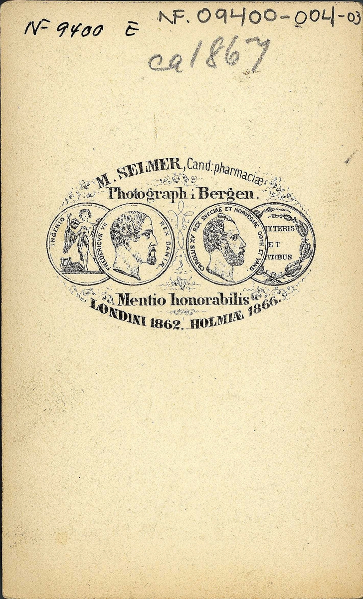 26. Konedrakt, Ullensvang. Portrett av kvinne (kone) som sitter i fotoatelier og støtter seg på et møbel med mønstret gulvteppe under. Del av serien "Norske Nationaldragter"  (nr.26) av fotograf Marcus Selmer (1819-1900), Bergen.