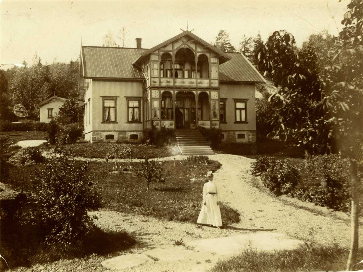 Sætre gård, Heggedal, Asker, Akershus. Våningshus i sveitserstil med glassveranda, hvitkledd kvinne i hagen