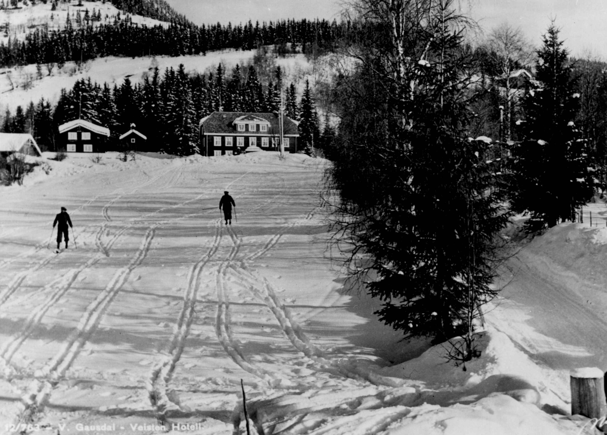 Avfotografert postkort. To skiløpere på ski i snødekt landskap foran Veisten hotell i Vestre Gausdal.