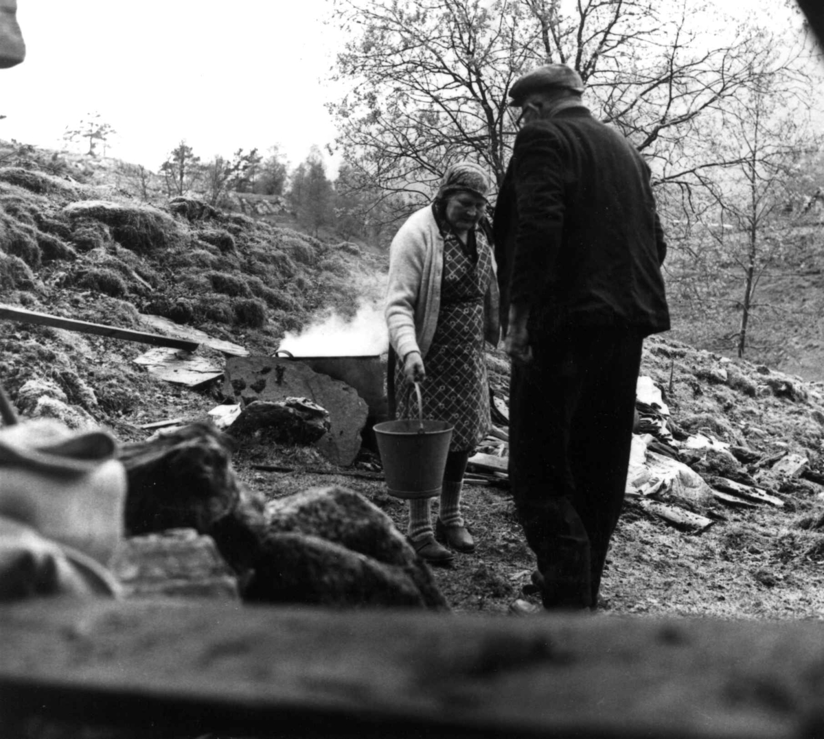 Stamping av vadmel. Serina Kvæstad bærer vann til vadmelstøyet, Ingemund Kvæstad i forgrunnen. Kvæstad, Suldal, Rogaland 1970.