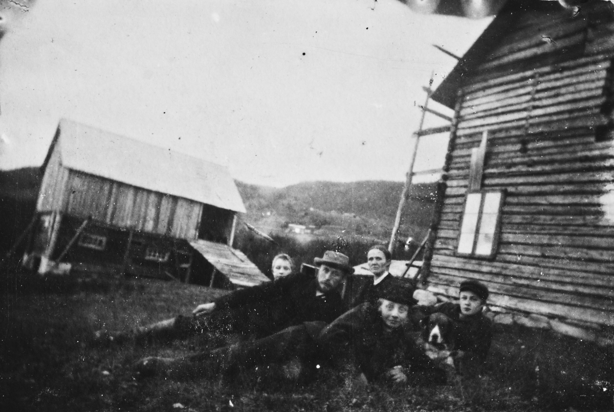 Familiegruppe på gårdstun, Fossum gård, Hauggrend, Fyresdal, Telemark. Signe Maline Quisling (bak) giftet seg i 1873 med Jon Gunnarson (med hatt), lærer,  kirkesanger og spillemann, fra Øvre Midtgarden, Hauggrend. De bosatte seg på denne gården og tok navnet Fossum. Sønnene var  Gunnar Torbjørn til venstre og Lars Abraham til høyre, mens gutten foran er deres fetter Gunnar Midtgarden som etterhvert overtok farsgården Øvre Midtgarden. Bildet er tatt innen 1889 da Jon G. F. dro til Amerika.