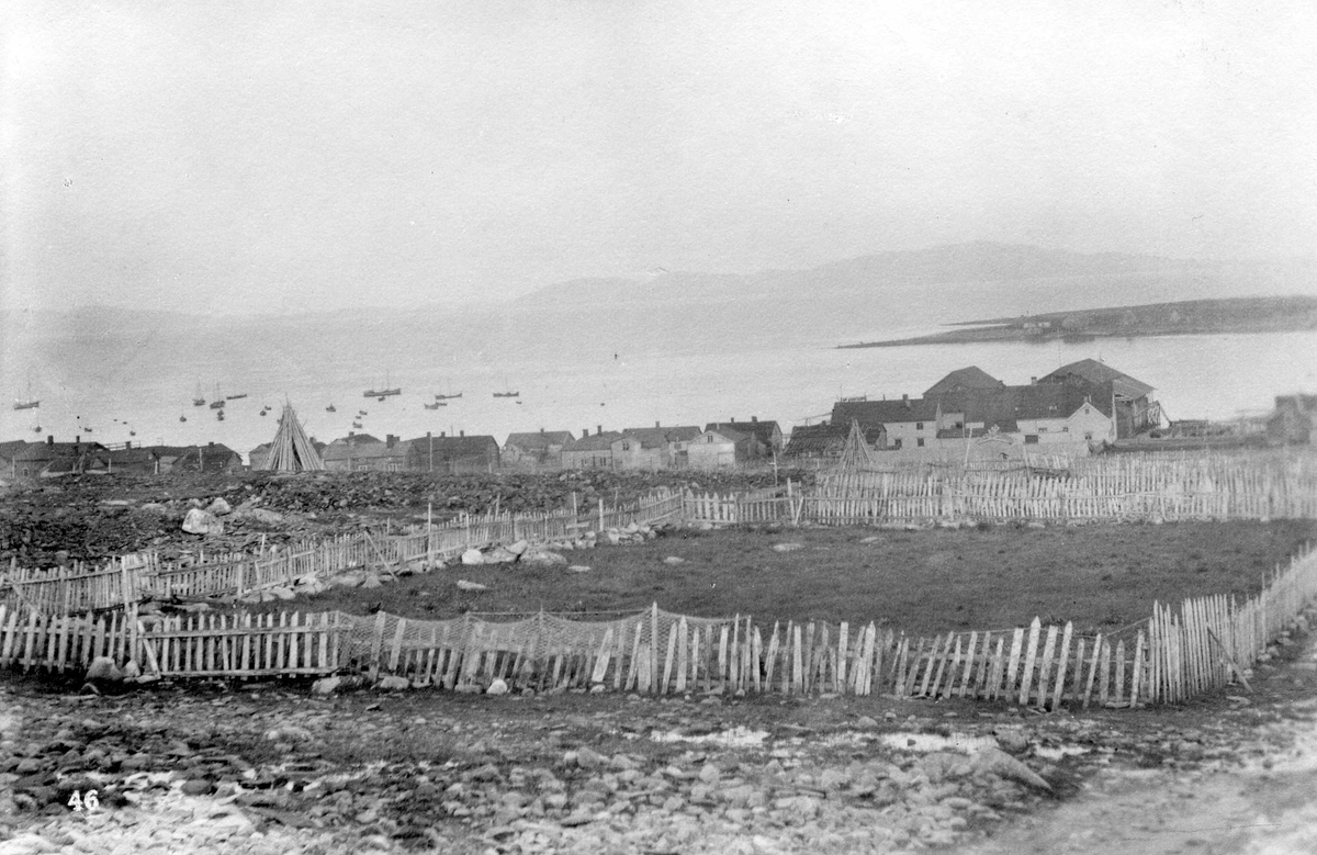 Vadsø. Innhegning forann bebyggelse mot fjord og båter.