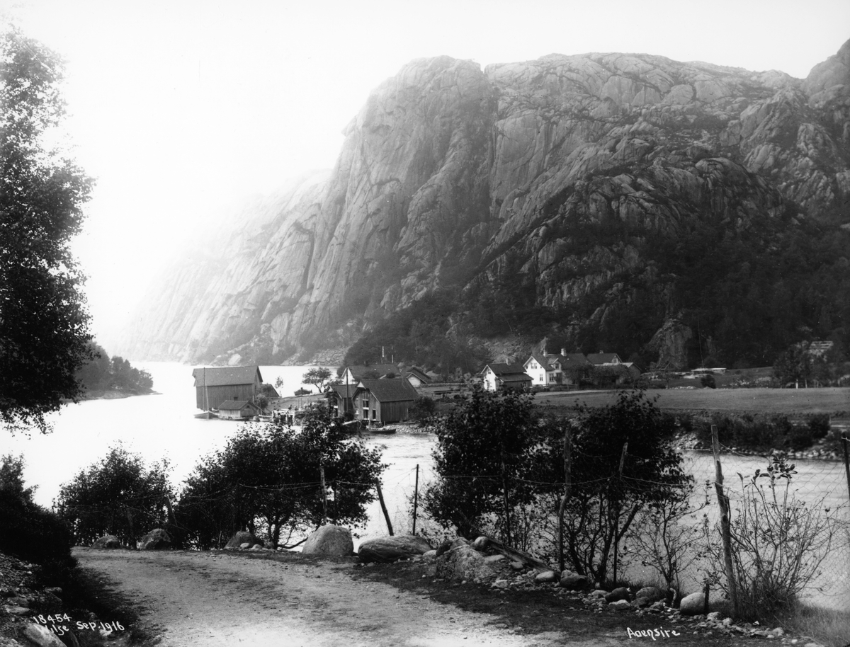 Landskap, med fjell- og fjordparti og bebyggelse, Åna-Sira, Sokndal, Rogaland. Flere gårdsbruk, bryggepartier med sjøboder. Veiparti i forgrunnen.