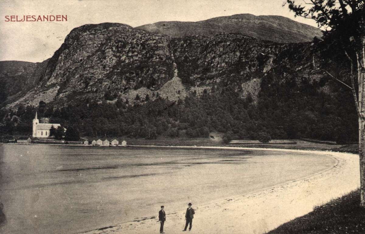 Postkort. Jule. og nyttårshilsen. Foto svart/hvitt. Motiv fra Seljesanden. Kirke. Fjell. Sandstrand. Datert 23.12.1907.