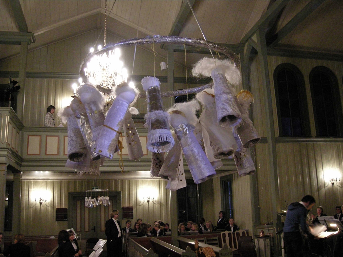 Adventssamling og julekonsert i Birkenes kirke, Aust-Agder, 16.12.2007. Krans med engler laget av barn i 1.trinn ved Birkenes skole. Gjøres hvert år og kirken betaler for materialer. Rockering og vevgarnsvindsler kledd med aluminiumsfolie, englene pyntet med bånd, stoff og bomull.