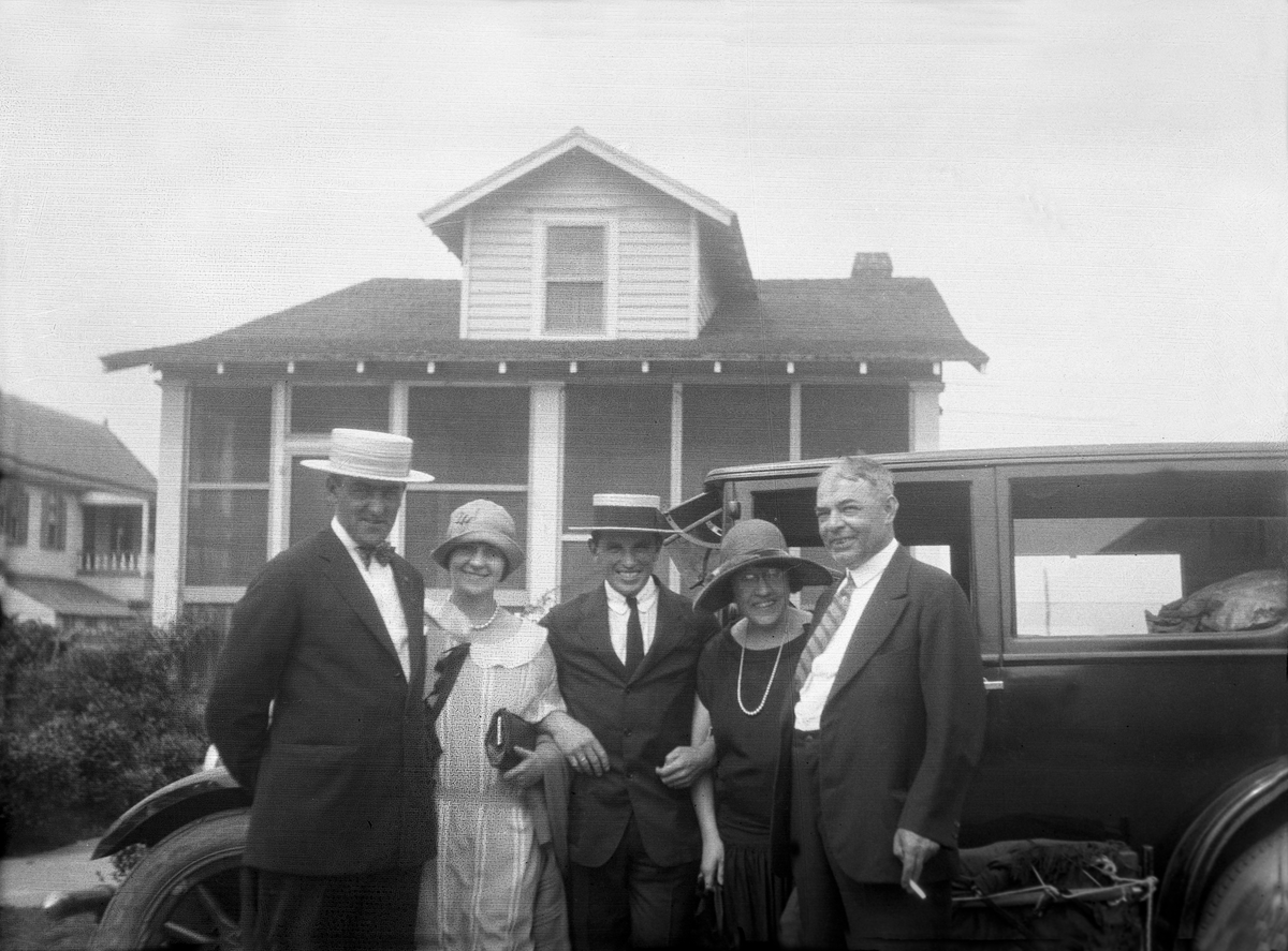 Jack, en hushjelp, Fritjof Arentz, fru Johnsen og dr. Johnsen står for en bil med et hus i bakgrunn, Philadelphia, USA. Fotografert 1926. Fritjof Arentz arbeidet 1 år i Philadelphia.