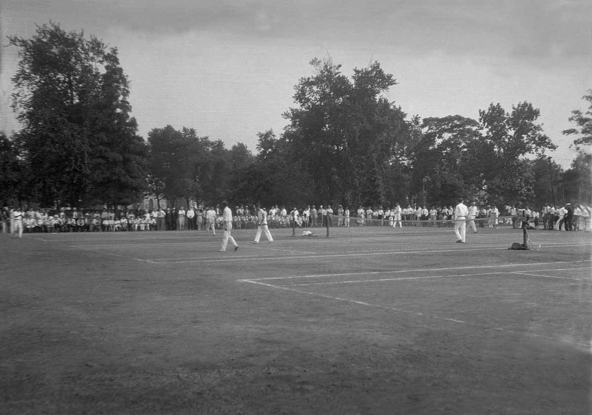 Flere spiller spiller på tennisbanen, publikum står rundt banen, Richmond Park, London.