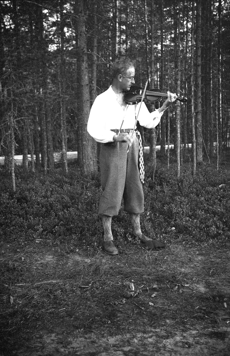 Olaf Gunderson senior spiller på en fele i skogen. Fotografert 1934.