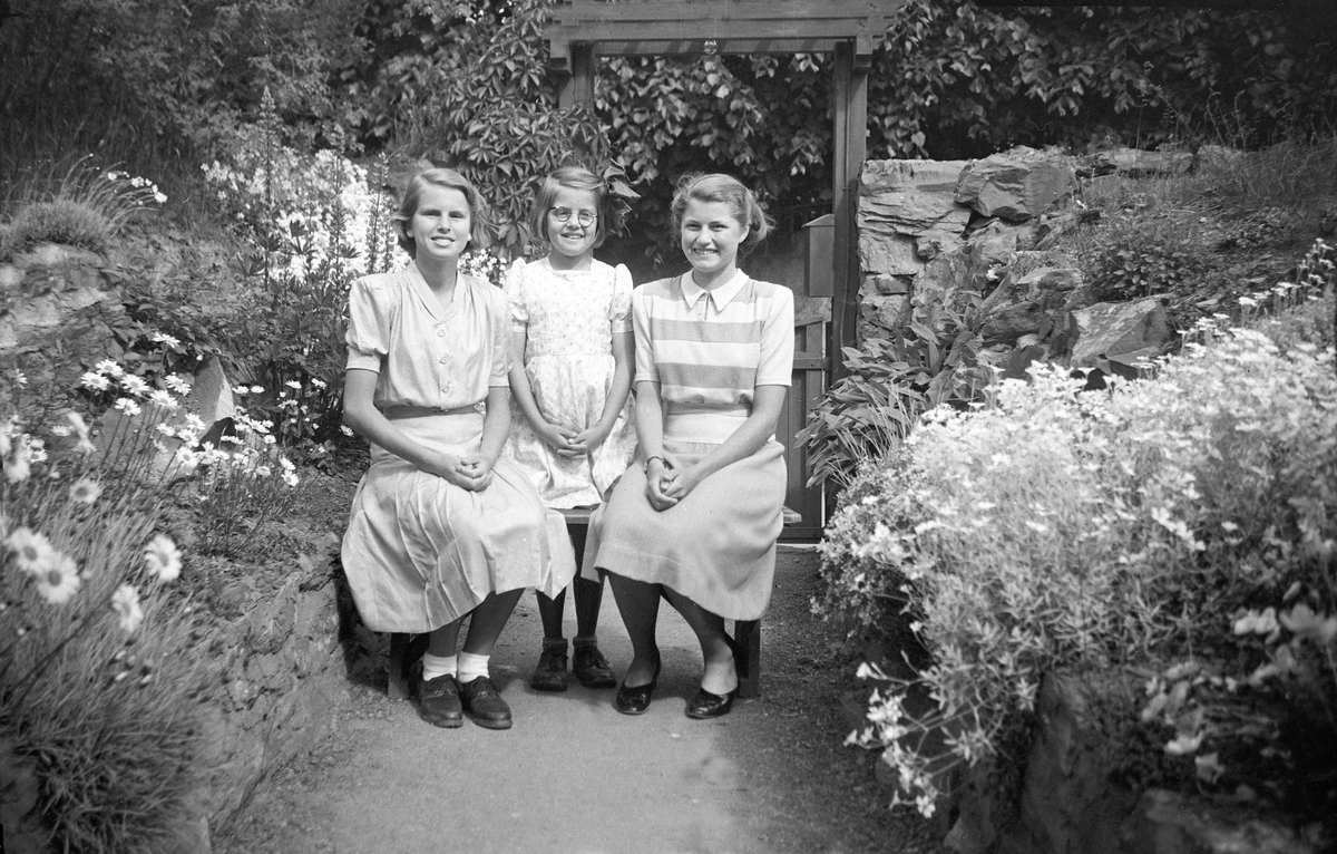 Søstrene Siri, Kari og Guri Arentz sitter på en benk i hagen i P.T. Mallingsvei 4, Bygdøy.  Fotografert 14. juni 1946.