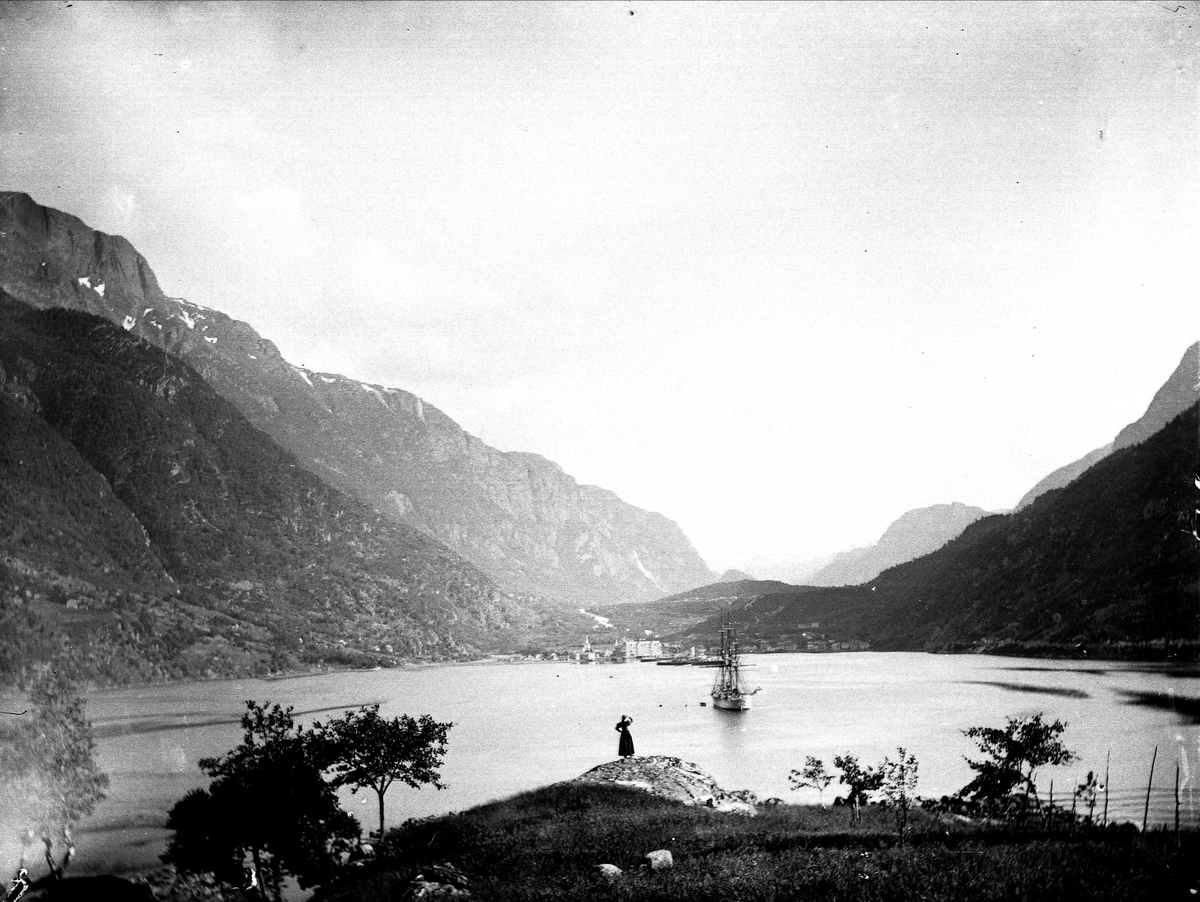 Landskapsfotografi fra Odda i Hardanger. I forgrunnen sees Sørfjorden med seileskute og i bakgrunnen fjell. 