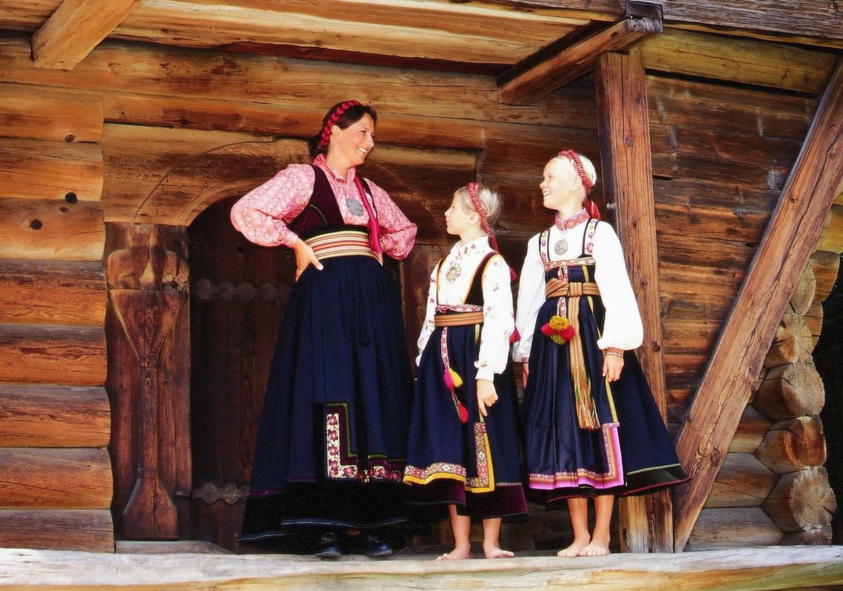 Kvinne og to jenter i telemarksbunad foran loftet fra Søndre Tveito,
bygning nr. 133 i Telemarkstunet på Norsk Folkemuseum.