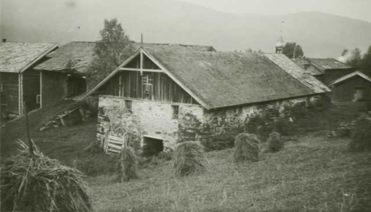 Gårdstun med steinfjøs,  Søstu Westgaard, Stor-Elvdal, Hedmark. Jorde med høystakker i forgrunnen.