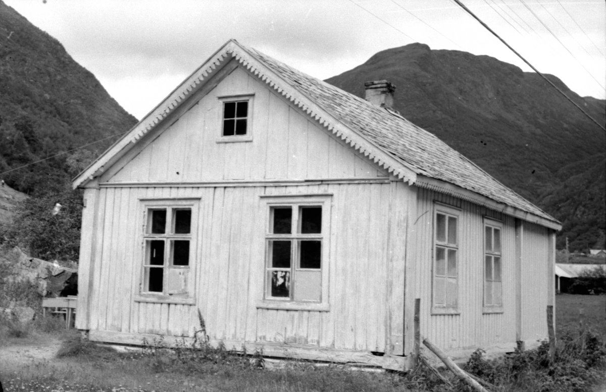 Berge (Øvre Kvamme), Borgund, Lærdal, Sogn og Fjordane, bygd 1872. Lite hvitt skolehus sett mot kortveggen, fjell i bakgrunnen. Lampe på hushjørnet. Registrering utført 1958-59 av Johan Schiong for Noregs Lærarlag. 