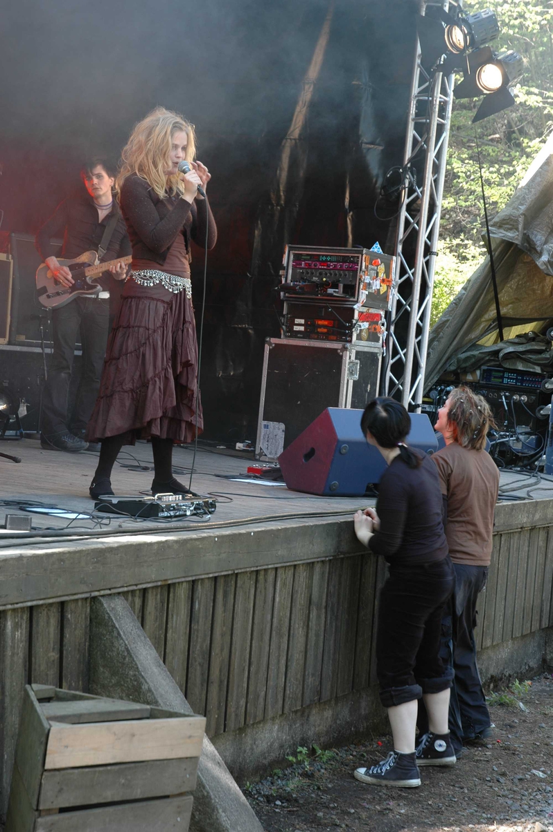 Musikkgruppen "Gåte", engasjert av Rikskonsertene, spiller for ca. 1000 ungdomsskole-elever per konsert, på friluftsteateret, nummer 349 på Norsk Folkemuseum  i mai 2005.To ivrige fans henger på scenekanten.