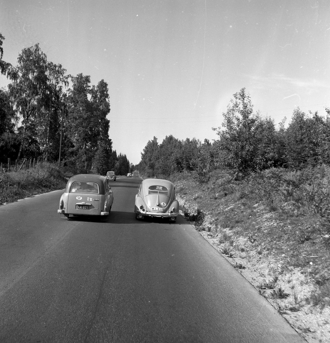 Langs Riksvei 1kjører det to biler ved siden av hverandre. Fotografert 7. juli 1958.