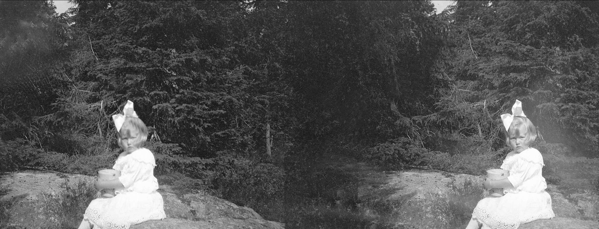 En jente sitter på en stein i skogen og holder en spann i hendene. Robsahm og Lund. Stereofotografi (negativ)