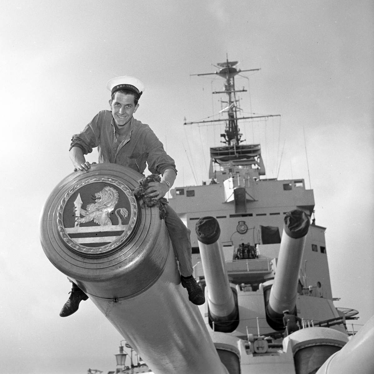 Serie. Det engelske slagskipet HMS Vanguard på flåtebesøk i Oslo. Parade med musikkorps ombord. Noen av mannskapet står med kikkerter og en pusser kanoner. Fotografert 21. juni 1954.