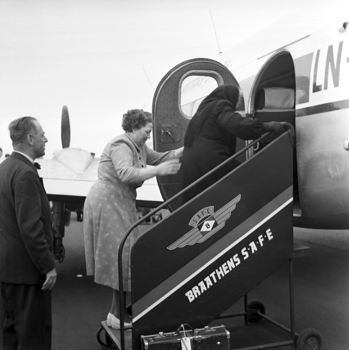 Serie. Før og under åpningen av Vigra flyplass. Mange arbeider rundt på området, noen menn står samlet og passasjerer går ombord på et Braathens safe fly. En dame står ved oppvaskbenken.  Fotografert juni 1958.