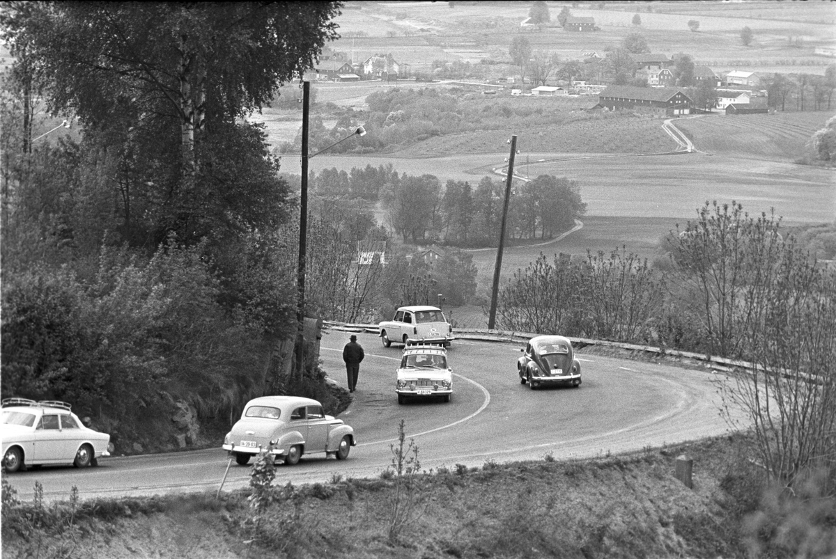 En mann går nedover Lierbakkenen med biler i begge retninger. (Bilene lengst til venstre: Volvo Amazon og Opel Olympia) Fotografert  juni 1961.