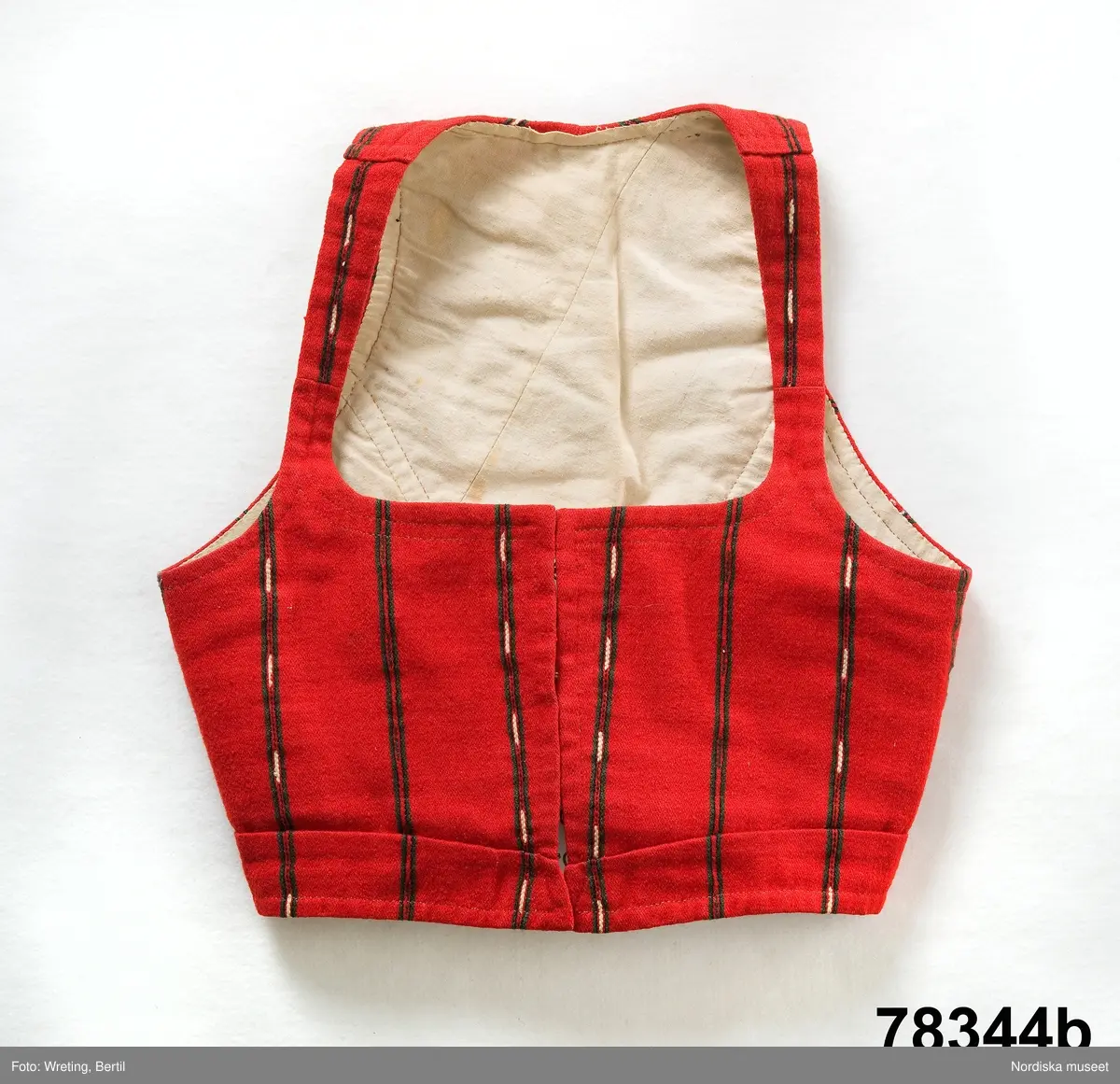 Huvudliggaren:
"Kvinnodräkt fr. Delsbo sn, Norra Helsinglands fgd, Helsingland.
a. "Ryntjeskjortel" af svart kläde med röd kant och bandväfd "kval" (linning). Kjolen "lurad"(goffrerad), skall förvaras lurad att ej vecken gå ut. 3 par fruntimmershänder hjälpas åt att "lura" den efter hvarje begagnande.
b. livstycke, rött med gröna ränder.
c. "Ryntjessärk" (rynksärk) af hvitt bomullstyg med "krus" (handbroderi) kring hals och händer.Begagnas sommartiden
d. "Bumsförkläde" af ylle, blårandigt med bandväf,"kval" i rödt och grönt.
e. "Förklesband" rödt och grönt ylle med "doppar" (tofsar) i ändarna. Lindas 1 à 2 hvarf kring lifvet och bindes framtill med stora nedhängande "locor" och ändar. Längd 262 cm, bredd 3,4 cm.
f. Kjolsäck med mässingslås och hake samt tennbroderi. Häktas under förklesbandet och hänger delvis under "försklet". Begagnas vanligen till förvaring af kyrkkryddor m.fl. kyrk-ellerkalassaker.
g. Halfhandskar af svart kläde med silkesbroderi. Begagnas sommartiden.
h. "Påshufva" hvardagsmössa af brokigt kattun. Begagnas med i nacken utslaget hår med några hårtestar hängande fritt framför öronen.
Till dräkten användes röda strumpor samt låga skor med höga klackar. Äfven kan användas silfersmycken kring halsen eller å  bröstet. En á två brokiga silkesdukar brukades omkring halsen nedstoppade under lifstycket, så att kruset kring halsen  på "ryntjessärken" sammanfästadt med ett löfspänne samt en smalare kant af hvarje sidenduk, blevo synliga. Vid handlederna sammanfästes ryntjessärken med röda sidenband eller länkknappar.

a. KJOL 
längd: 87 cm
midjeband bredd: 7 cm
av svart halvylle med svart linvarp och inslag av svart 1-tr. ullgarn, de 2 yttersta stadtrådarna är av oblekt lingarn. 4 goffrerade våder samt en slät framvåd som skarvats under förklädet med oblekt bomullslärft. 5 cm bred list av rött kläde i nederkanten runtom. Brett midjeband mönstervävt i rött och grönt ullgarn och vitt bomullsgarn. Knäppt vid framvådens vänstra sida med 2 hakar och hyskor av mässing.
b. LIVSTYCKE
längd: 39 cm
av halvylle i varptäckande kypert, varp av vitt lingarn, inslag av svart och grönt ullgarn med flaminslag av vitt, 2 fram-och sidstycken, 2 bakstycken avsmalnande till skörtveck med tre par tränsade förstärkningar av svart garn. I midjehöjd ett avsytt veck runtom, knäppt kant i kant med 8 par grova hakar och hyskor av mässing. Foder av ofärgad bomullslärft.
BE

c. ÖVERDEL
Längd: 39 cm. Längd: 58 cm - ärmlängd. Vidd: 56 cm - ärmvidd. Vidd: 114 cm. Höjd: 1,7 cm - kraghöjd. Material: Textil, bomull. Textil, linne - ärmlinning, krage. Bomullsgarn - broderi. Telnik: Tuskaft. Trådbundet broderi. Broderi, rätlinjig plattsöm. Handsömnad.
Överdel av tuskaftat vitt bomullstyg. Dubbelvikt bålstycke, isydda rektangulära halsspjäll. Täta breda stripade  rynkor mot halskrage i bomull, 1,7 cm hög. Kragen har broderier i rätlinjig plattsöm, vitt bomullsgarn över hela ytan, nuggor i kanten, langetterade bågar  i framkant. 16 cm långt sprund fram, tränsad förstärkning nedtill, 3 cm.  Vidsydd ärm med  infällda ärmspjäll, lagda veck över axeln fram och bak. Täta breda stripade rynkor mot 2,5 cm bred ärmlinning. Ärmlinningen har yttäckande vita broderier i rätlinjig plattsöm, rombiska former. Vita knytband i bomull i ärmlinningar och krage. Överdelen är handsydd.
/Inga-Lill Eliasson 2007-11-26


d. FÖRKLÄDE
längd=vådbredd: 82 cm
bredd: 97,5 cm
av halvylle, varp av svart lingarn, inslag i varptäckande kypert av svart 1-tr. ullgarn med smala ränder istarkt blått och en knappt synlig svart tråd med vita flamgarnsfläckar av bomull. Upptill stripade rynkor där de blå bårderna utnyttjats dekorativt i rynkningen. Mönstervävt midjeband i grönt på rött ullgarn , bandet knäpps med 2 hakar och hyskor i vänster sida.
I nederkantens båda hörn infodringar på insidan av svart bomullslärft, för att tyget inte skall rulla sig.



Berit Eldvik 2004