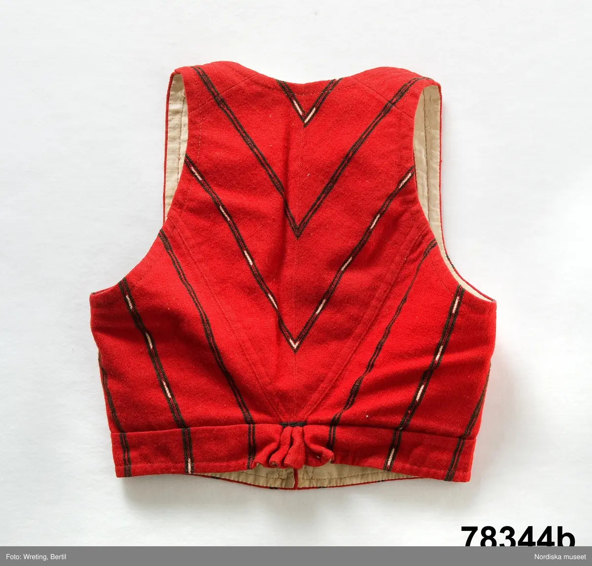 Huvudliggaren:
"Kvinnodräkt fr. Delsbo sn, Norra Helsinglands fgd, Helsingland.
a. "Ryntjeskjortel" af svart kläde med röd kant och bandväfd "kval" (linning). Kjolen "lurad"(goffrerad), skall förvaras lurad att ej vecken gå ut. 3 par fruntimmershänder hjälpas åt att "lura" den efter hvarje begagnande.
b. livstycke, rött med gröna ränder.
c. "Ryntjessärk" (rynksärk) af hvitt bomullstyg med "krus" (handbroderi) kring hals och händer.Begagnas sommartiden
d. "Bumsförkläde" af ylle, blårandigt med bandväf,"kval" i rödt och grönt.
e. "Förklesband" rödt och grönt ylle med "doppar" (tofsar) i ändarna. Lindas 1 à 2 hvarf kring lifvet och bindes framtill med stora nedhängande "locor" och ändar. Längd 262 cm, bredd 3,4 cm.
f. Kjolsäck med mässingslås och hake samt tennbroderi. Häktas under förklesbandet och hänger delvis under "försklet". Begagnas vanligen till förvaring af kyrkkryddor m.fl. kyrk-ellerkalassaker.
g. Halfhandskar af svart kläde med silkesbroderi. Begagnas sommartiden.
h. "Påshufva" hvardagsmössa af brokigt kattun. Begagnas med i nacken utslaget hår med några hårtestar hängande fritt framför öronen.
Till dräkten användes röda strumpor samt låga skor med höga klackar. Äfven kan användas silfersmycken kring halsen eller å  bröstet. En á två brokiga silkesdukar brukades omkring halsen nedstoppade under lifstycket, så att kruset kring halsen  på "ryntjessärken" sammanfästadt med ett löfspänne samt en smalare kant af hvarje sidenduk, blevo synliga. Vid handlederna sammanfästes ryntjessärken med röda sidenband eller länkknappar.

a. KJOL 
längd: 87 cm
midjeband bredd: 7 cm
av svart halvylle med svart linvarp och inslag av svart 1-tr. ullgarn, de 2 yttersta stadtrådarna är av oblekt lingarn. 4 goffrerade våder samt en slät framvåd som skarvats under förklädet med oblekt bomullslärft. 5 cm bred list av rött kläde i nederkanten runtom. Brett midjeband mönstervävt i rött och grönt ullgarn och vitt bomullsgarn. Knäppt vid framvådens vänstra sida med 2 hakar och hyskor av mässing.
b. LIVSTYCKE
längd: 39 cm
av halvylle i varptäckande kypert, varp av vitt lingarn, inslag av svart och grönt ullgarn med flaminslag av vitt, 2 fram-och sidstycken, 2 bakstycken avsmalnande till skörtveck med tre par tränsade förstärkningar av svart garn. I midjehöjd ett avsytt veck runtom, knäppt kant i kant med 8 par grova hakar och hyskor av mässing. Foder av ofärgad bomullslärft.
BE

c. ÖVERDEL
Längd: 39 cm. Längd: 58 cm - ärmlängd. Vidd: 56 cm - ärmvidd. Vidd: 114 cm. Höjd: 1,7 cm - kraghöjd. Material: Textil, bomull. Textil, linne - ärmlinning, krage. Bomullsgarn - broderi. Telnik: Tuskaft. Trådbundet broderi. Broderi, rätlinjig plattsöm. Handsömnad.
Överdel av tuskaftat vitt bomullstyg. Dubbelvikt bålstycke, isydda rektangulära halsspjäll. Täta breda stripade  rynkor mot halskrage i bomull, 1,7 cm hög. Kragen har broderier i rätlinjig plattsöm, vitt bomullsgarn över hela ytan, nuggor i kanten, langetterade bågar  i framkant. 16 cm långt sprund fram, tränsad förstärkning nedtill, 3 cm.  Vidsydd ärm med  infällda ärmspjäll, lagda veck över axeln fram och bak. Täta breda stripade rynkor mot 2,5 cm bred ärmlinning. Ärmlinningen har yttäckande vita broderier i rätlinjig plattsöm, rombiska former. Vita knytband i bomull i ärmlinningar och krage. Överdelen är handsydd.
/Inga-Lill Eliasson 2007-11-26


d. FÖRKLÄDE
längd=vådbredd: 82 cm
bredd: 97,5 cm
av halvylle, varp av svart lingarn, inslag i varptäckande kypert av svart 1-tr. ullgarn med smala ränder istarkt blått och en knappt synlig svart tråd med vita flamgarnsfläckar av bomull. Upptill stripade rynkor där de blå bårderna utnyttjats dekorativt i rynkningen. Mönstervävt midjeband i grönt på rött ullgarn , bandet knäpps med 2 hakar och hyskor i vänster sida.
I nederkantens båda hörn infodringar på insidan av svart bomullslärft, för att tyget inte skall rulla sig.



Berit Eldvik 2004