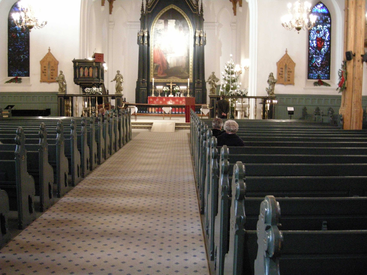 1. juledag i Kristiansand Domkirke, 25.12.2007. Oversiktsbilde fra kirkerommet før gudstjenesten. Kirkebenker, salmetavler, prekestol og alter med røde tekstiler, altertavle, juletre, glassmalerier, lysekroner. 