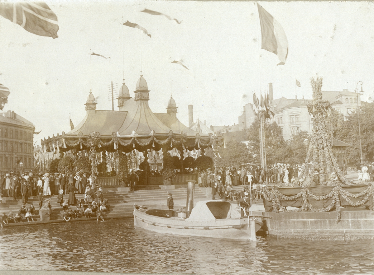 Serie med fire foto fra den franske prsidenten Clement Armand Fallières statsbesøk i Kristiania i 1908. Velkomstpaviljong med baldakin, pyntet med girlander og flagg. Dekorasjoner utført av B. Lange, antakelig. Tilskuere på Honnørbrygga i hovedstaden. Karl Johans gate er også pynytet med dekorasjoner.