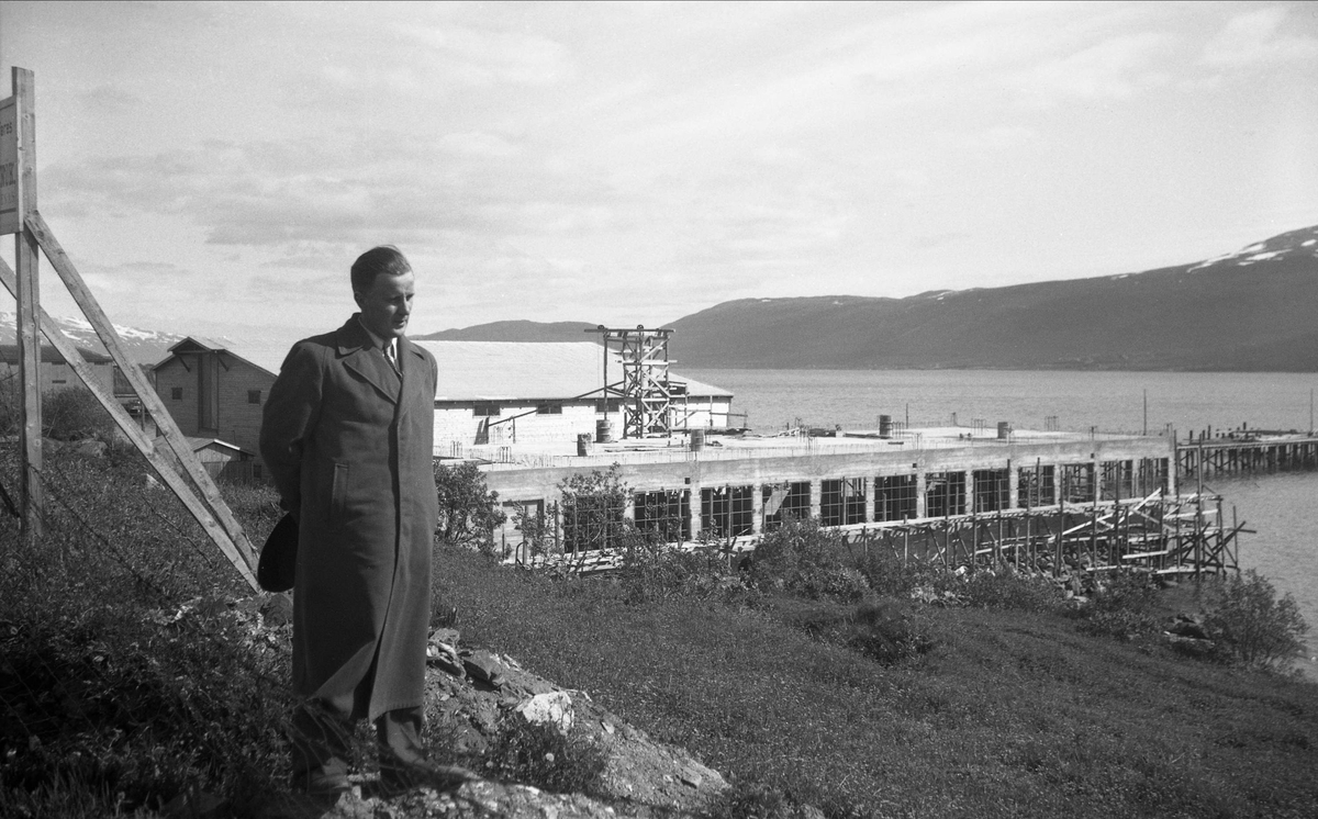 Ukjent mann foran industrianlegg ved sjøen i Tromsø. Bildet er tatt under reise med Hurtigruten i 1949.