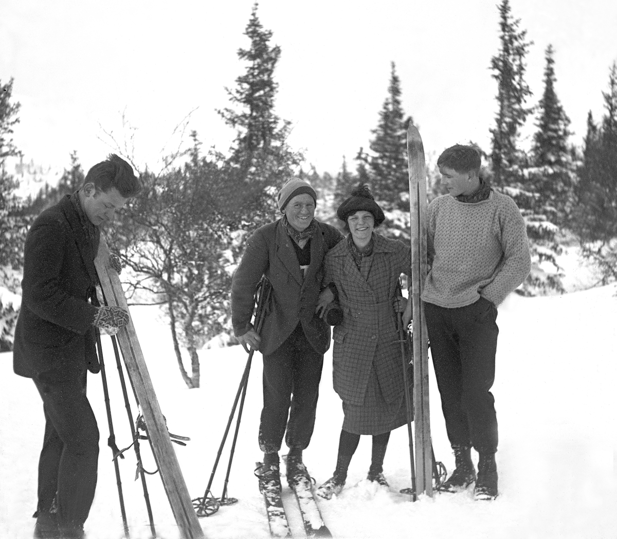 Tre unge menn og en kvinne med ski i vinterlandskap. Fotografert 1921.